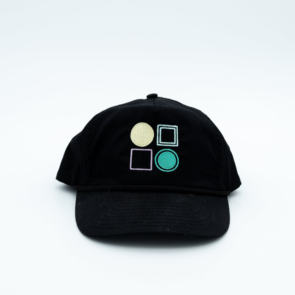 A black baseball cap featuring four embroidered geometric shapes on the front.