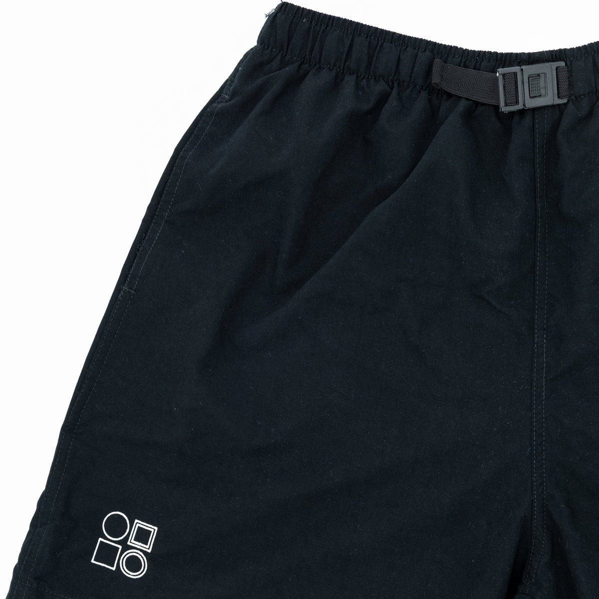 Black athletic shorts with an elastic waistband, a small white geometric logo on the lower left leg, and a black belt with a silver buckle.