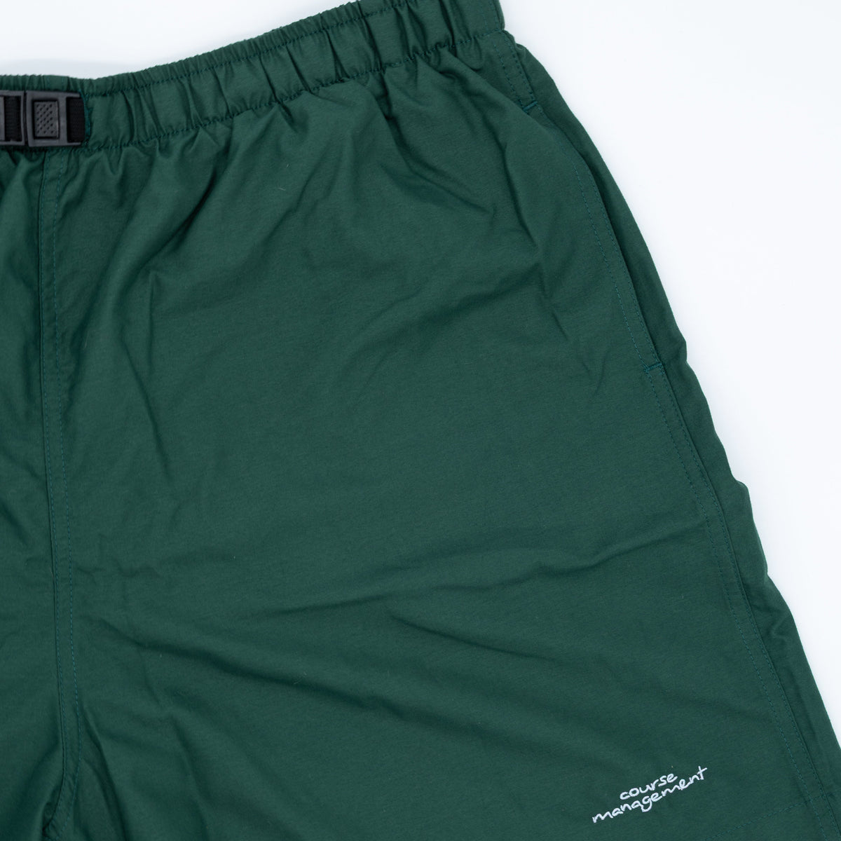 Dark green athletic shorts with an elastic waistband and a small white embroidered logo on the lower right leg, shown against a plain white background.