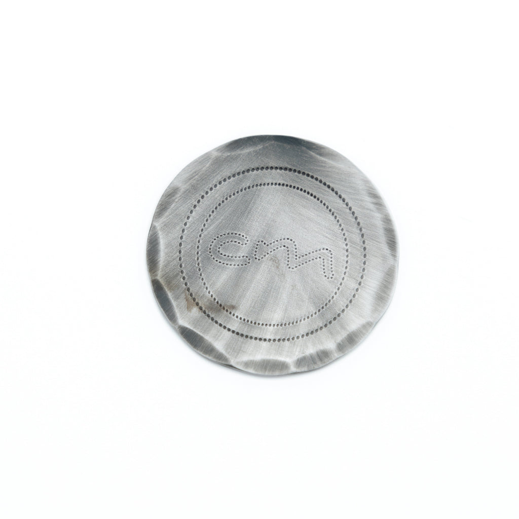 A round metallic ball mark with a brushed finish and a debossed monogram logo in the center, shown on a plain white background.