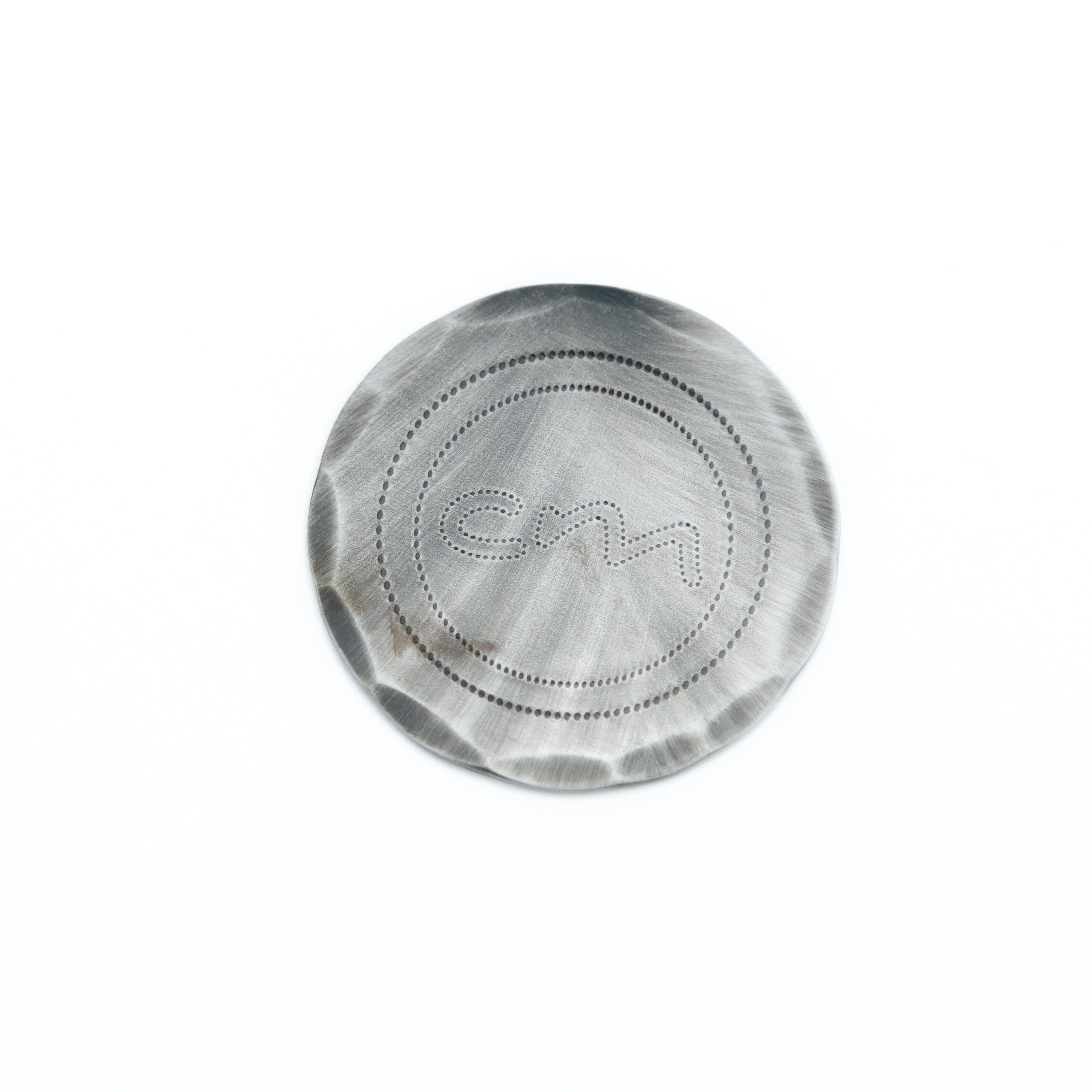 A round metallic ball mark with a brushed finish and a debossed monogram logo in the center, shown on a plain white background.