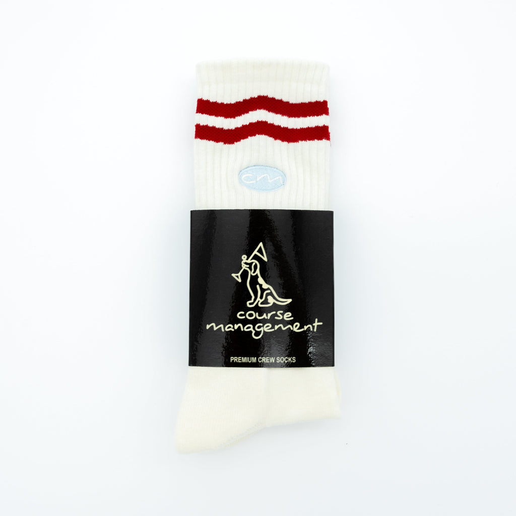 A pair of white crew socks with two red stripes near the top, wrapped in a black paper band featuring the brand name 'course management'.