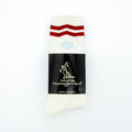 A pair of white crew socks with two red stripes near the top, wrapped in a black paper band featuring the brand name 'course management'.