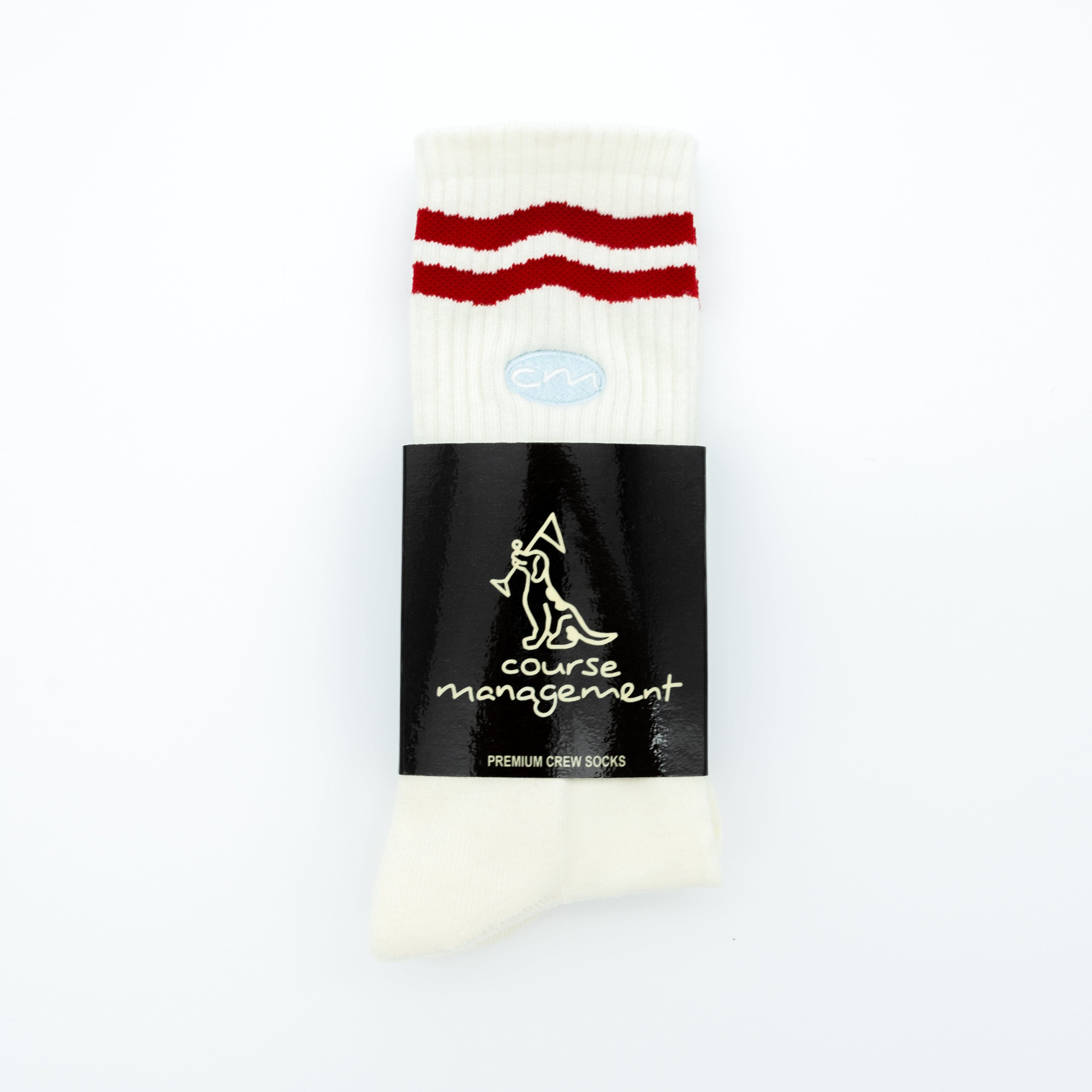A pair of white crew socks with two red stripes near the top, wrapped in a black paper band featuring the brand name 'course management'.
