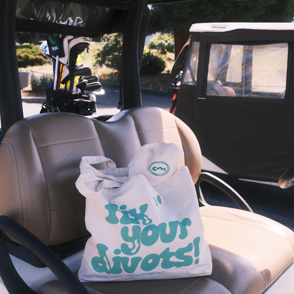 A tote with green text reading 'Fix your divots' resting on a beige car seat inside a golf cart.