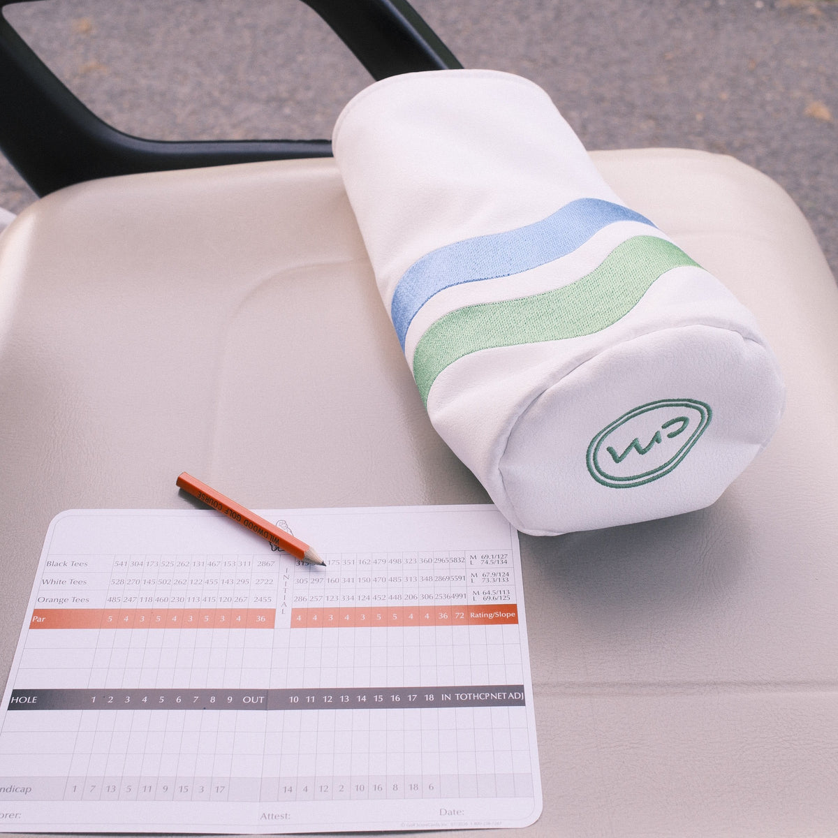 A golf club headcover resting on the back of a golf cart, alongside a scorecard and pencil, with an outdoor path in the background.