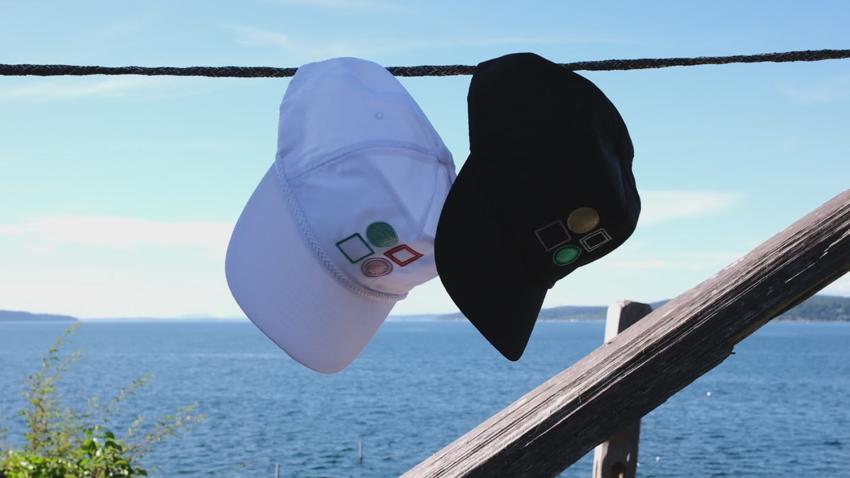 Two hats hang on a wire in front of the ocean.